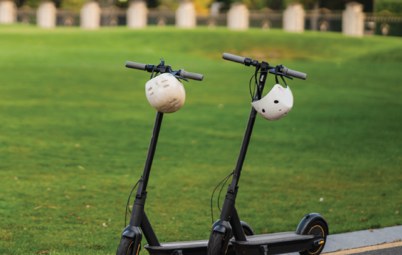 Two eScooters with helmets parked up in a park.